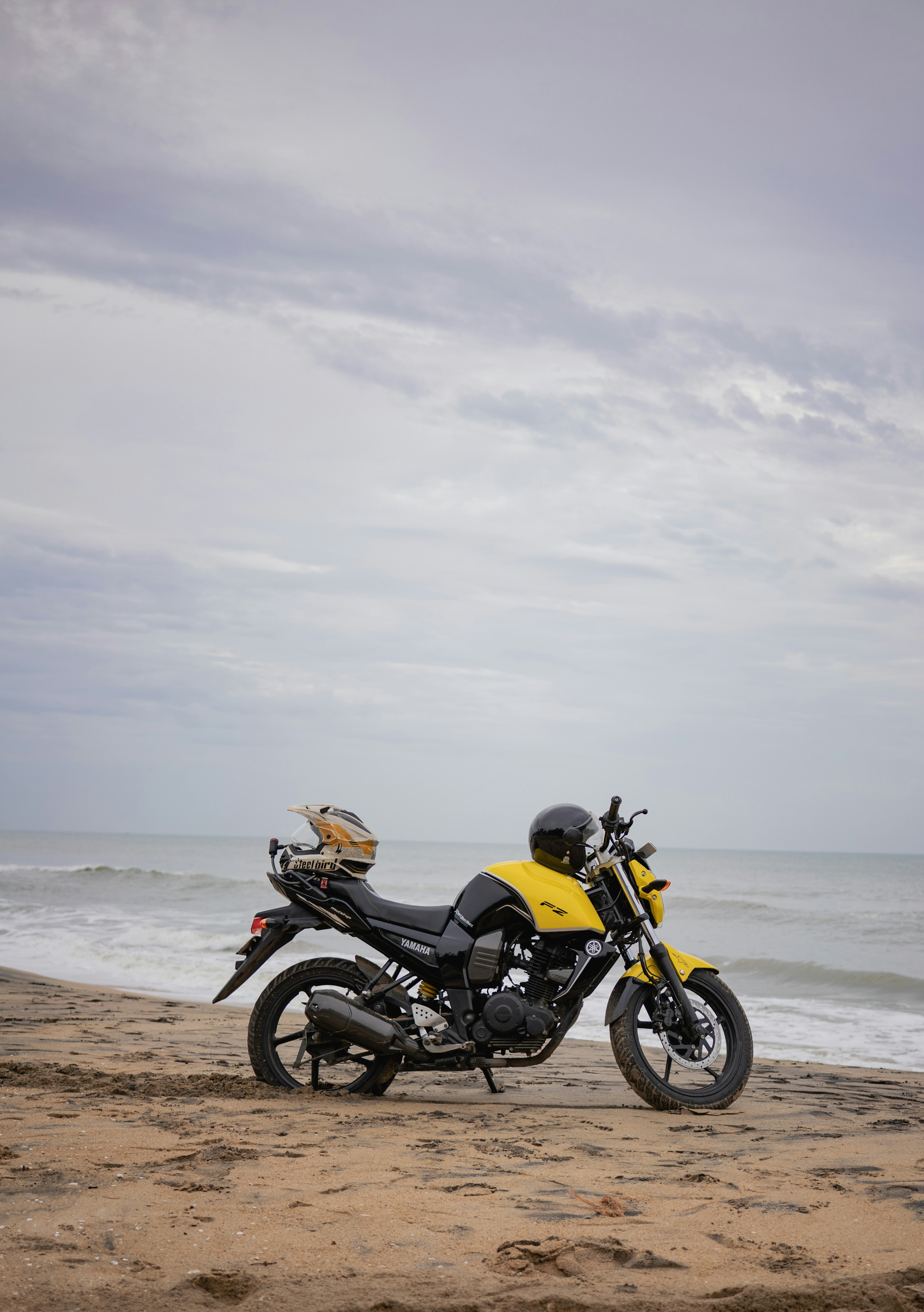 Yellow motorcycle parked on a sandy beach near ocean.