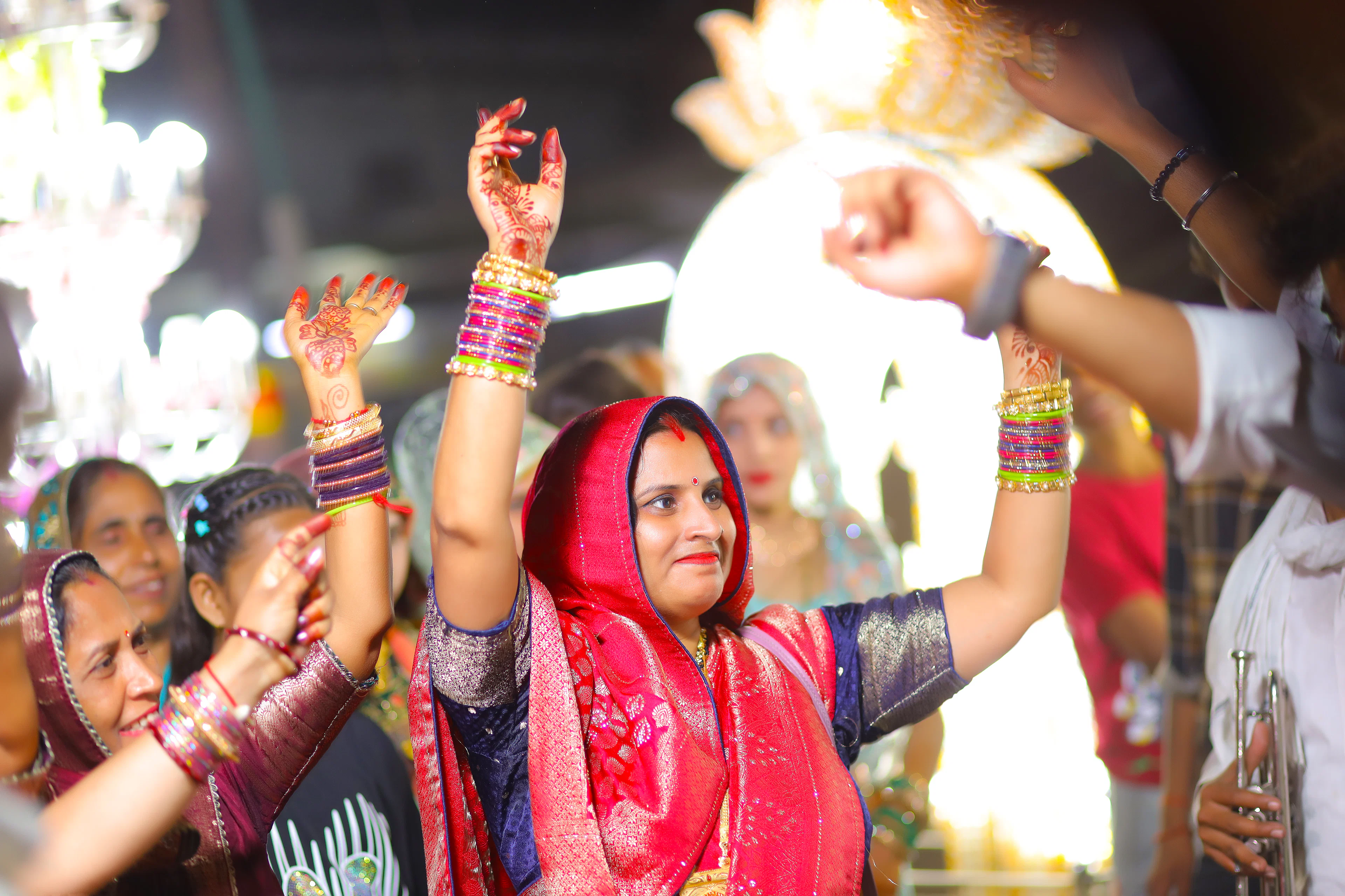 Women in bright saris dancing with raised hands at a sangeet