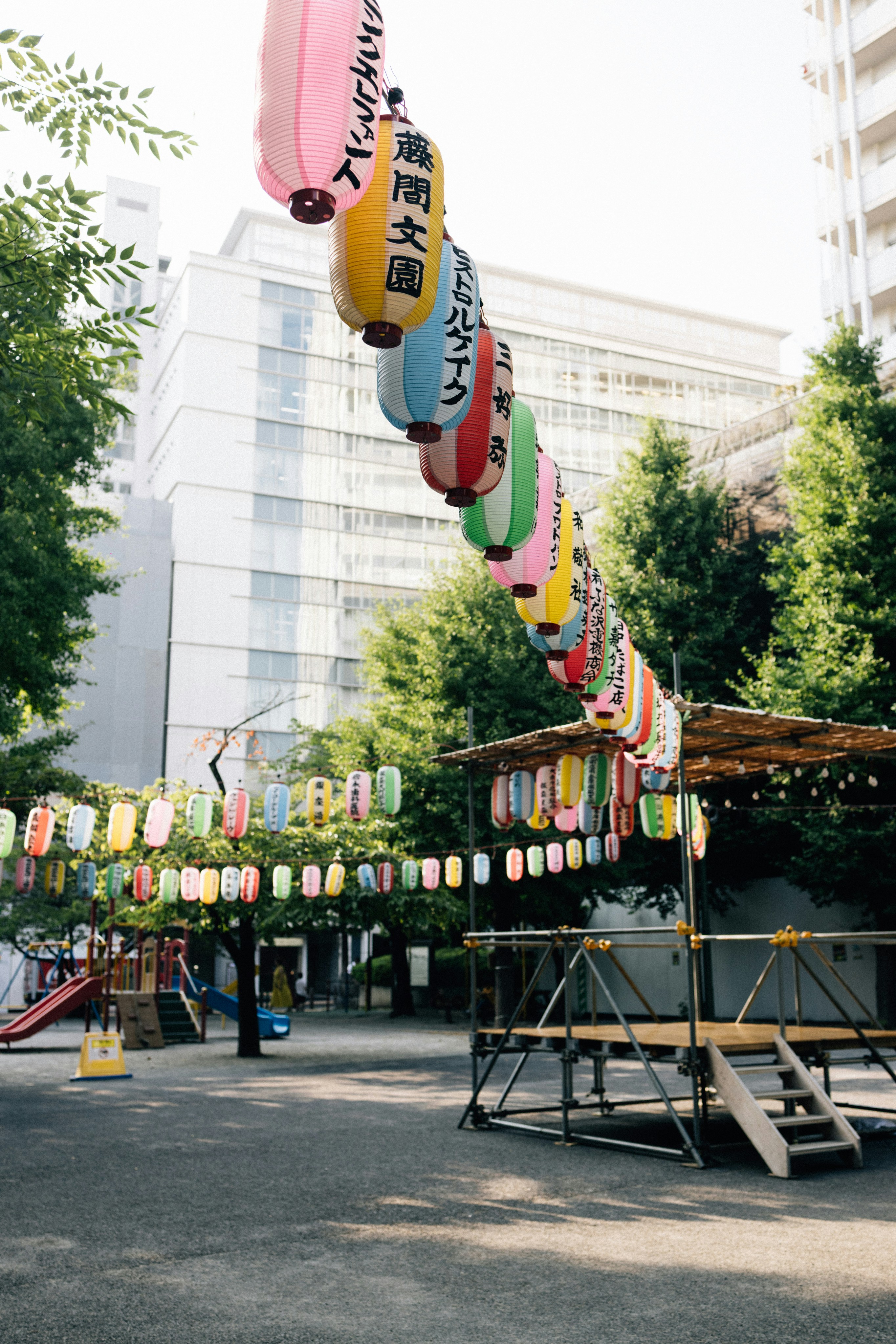 Colorful lanterns strung across a park with trees and buildings