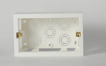 A white electrical back box with brass screws