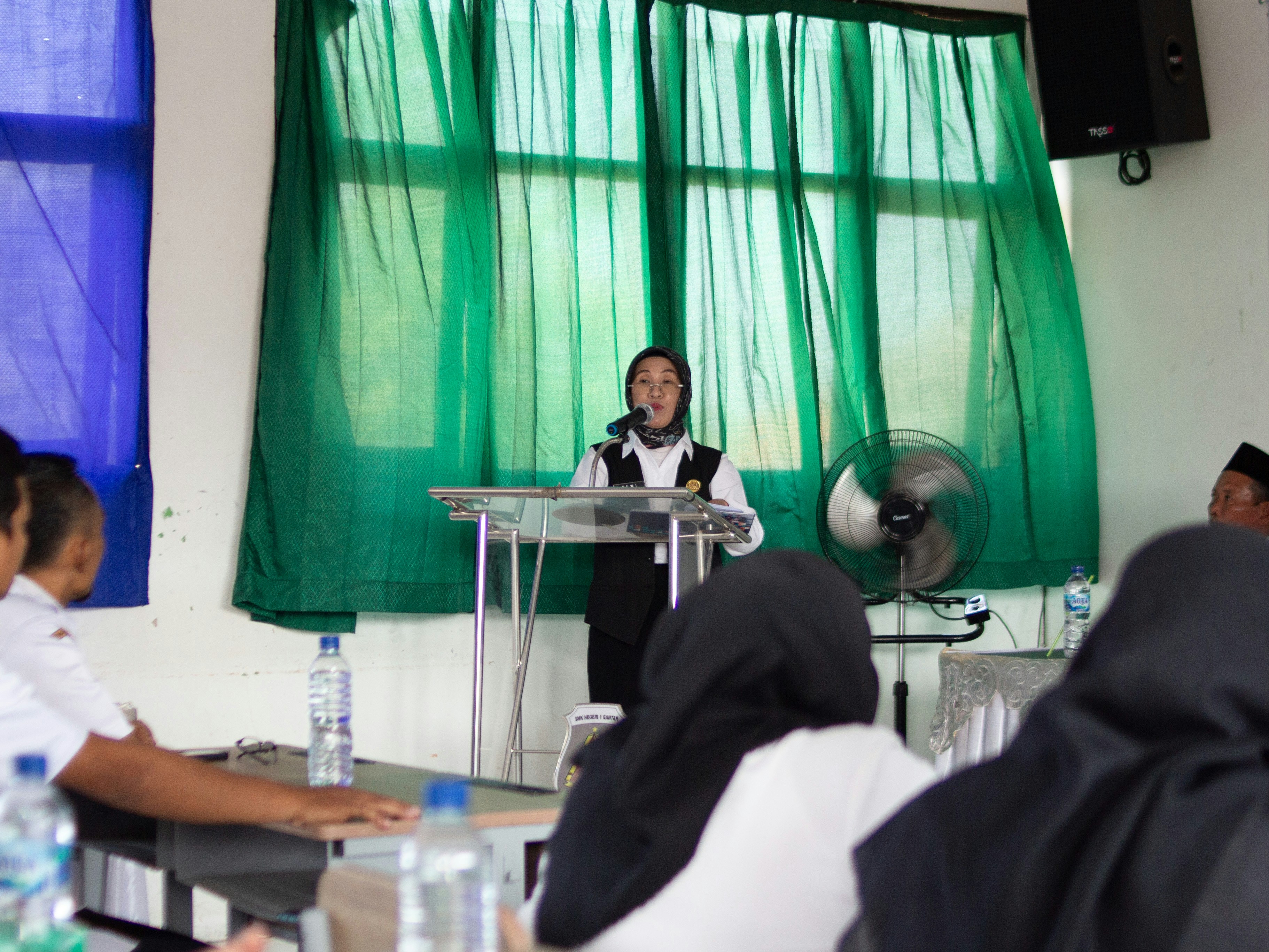 Woman delivering a speech at a podium with green drapes