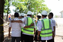 Construction workers in hard hats and vests huddle together.