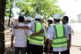 Construction workers in hard hats and vests huddle together.