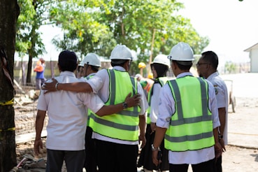 Construction workers in hard hats and vests huddle together.