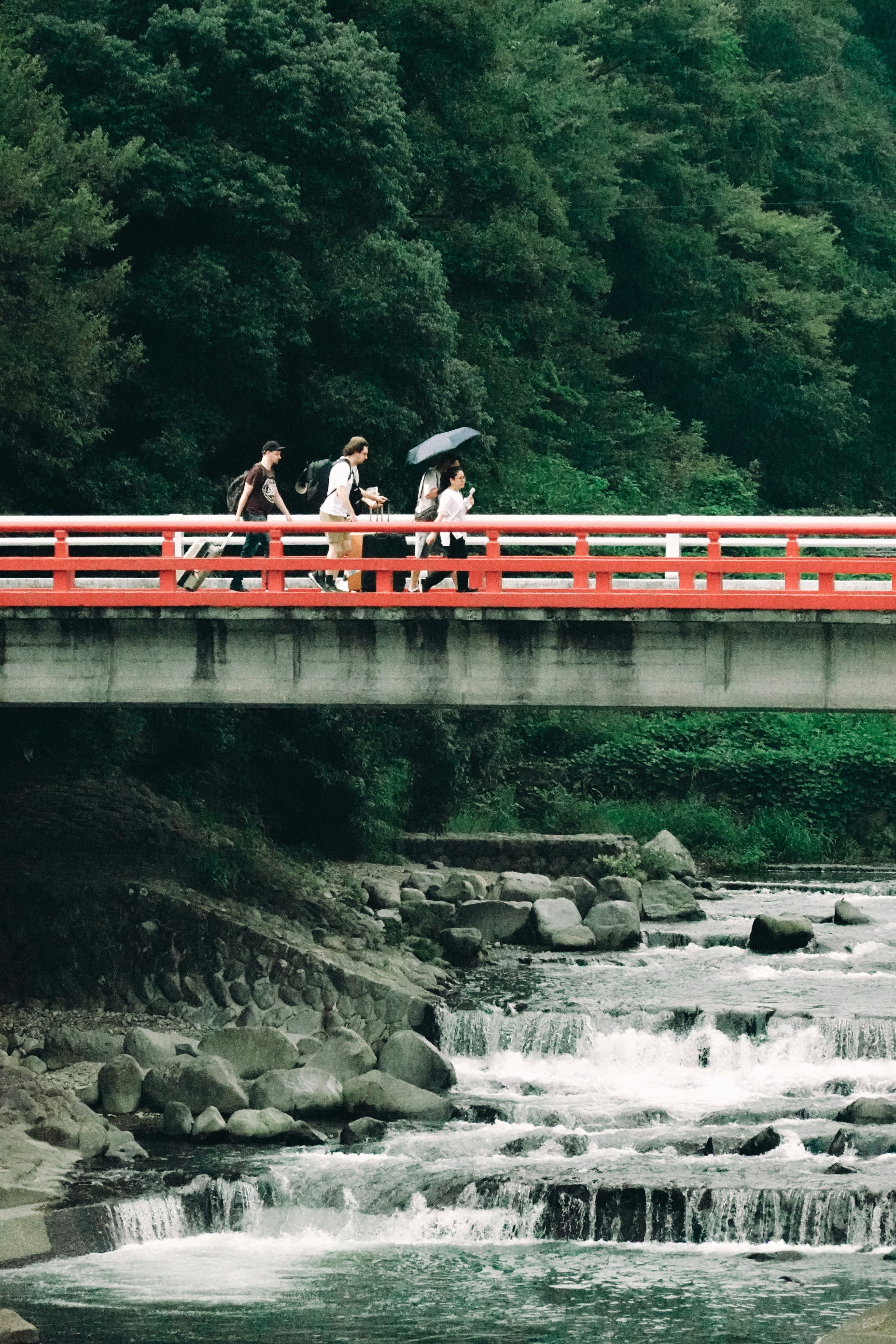 People walk across a red bridge over a river.