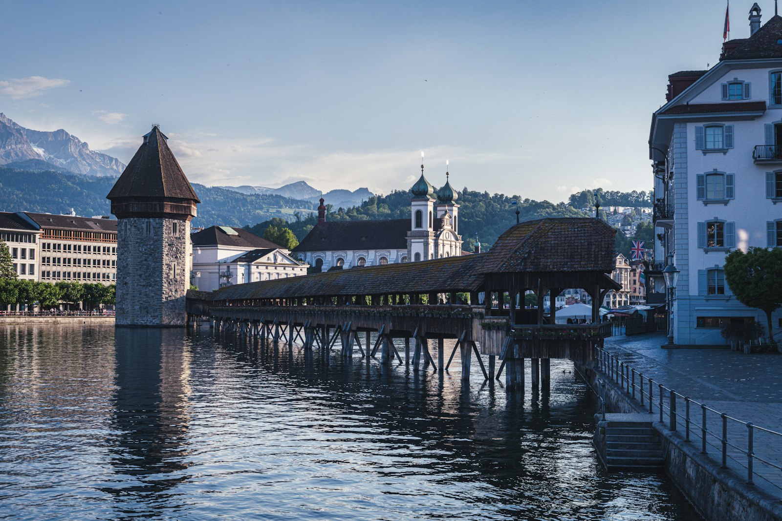 Lucerne's covered wooden Chapel Bridge and stone Water Tower on the Reuss River at dusk, with mountains beyond