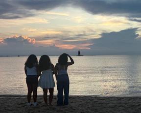 Three friends watch a sunset over the ocean.