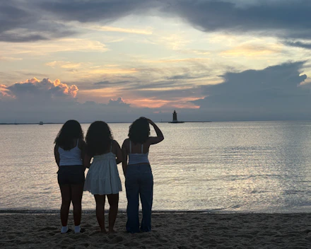 Three friends watch a sunset over the ocean.