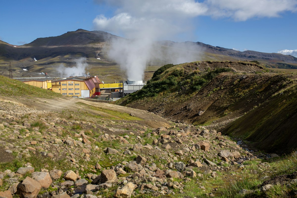 Geothermal steam rising from the earth beside industrial buildings