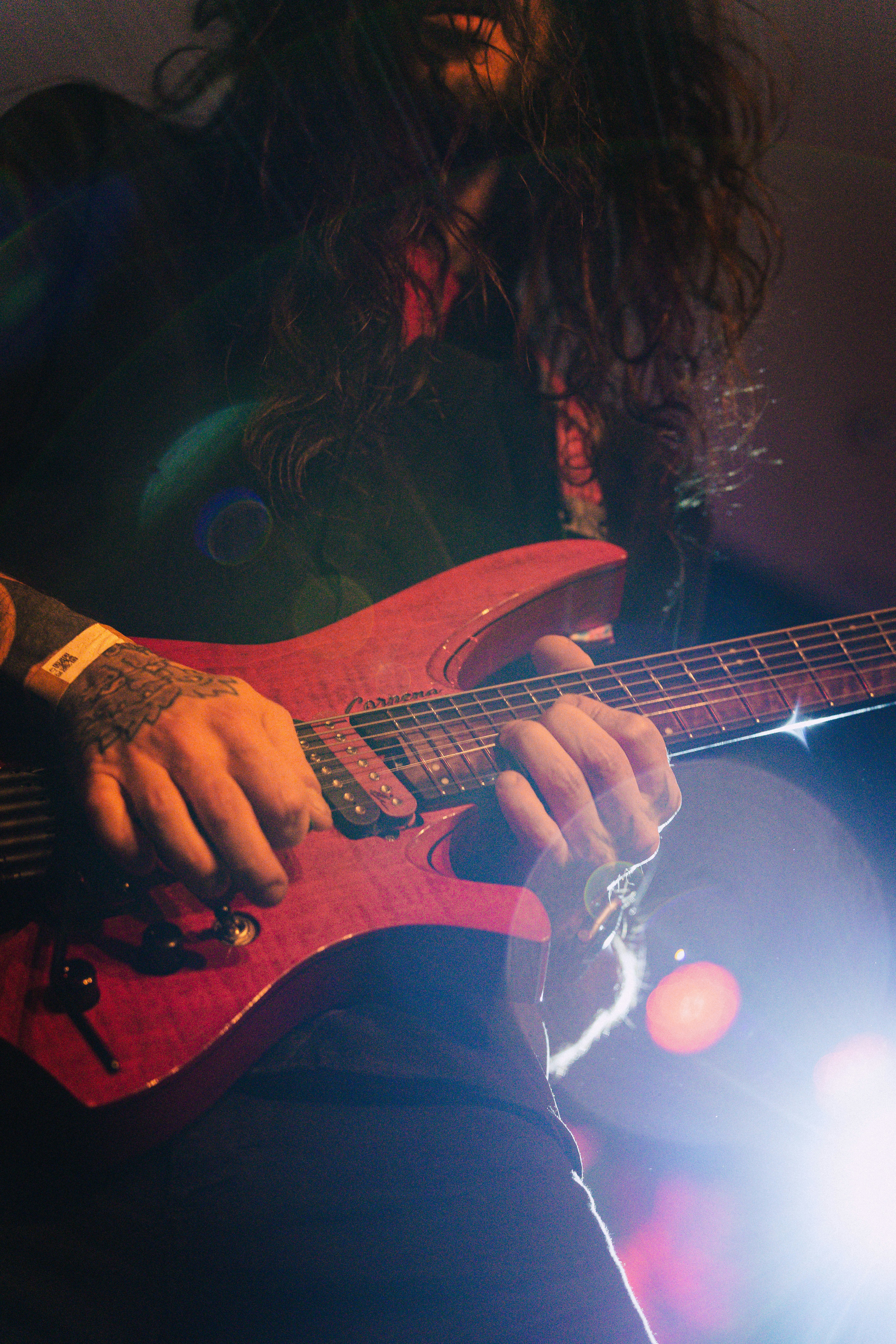Musician playing a red electric guitar on stage.