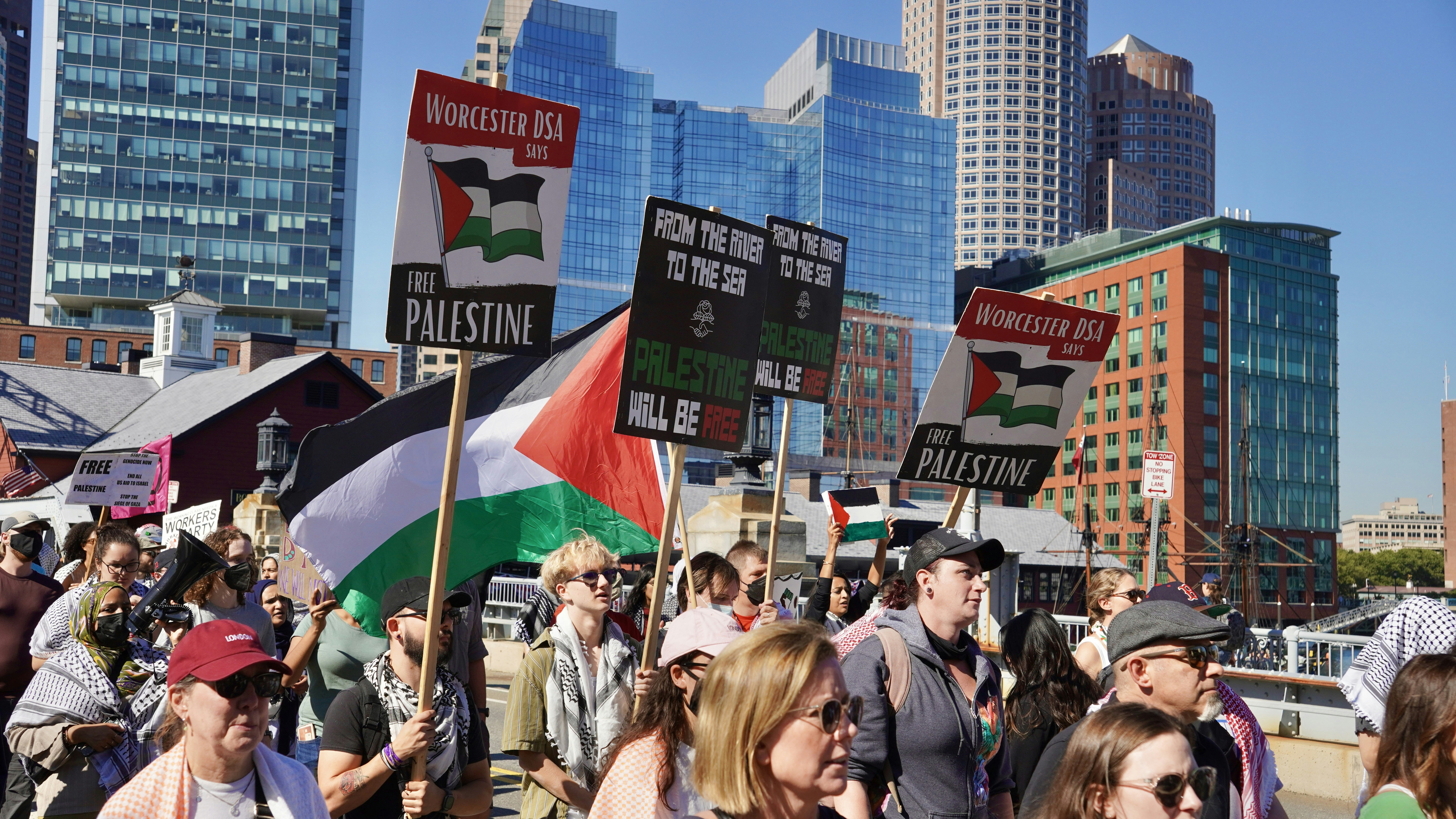 Protesters hold palestinian flags and signs in a city.