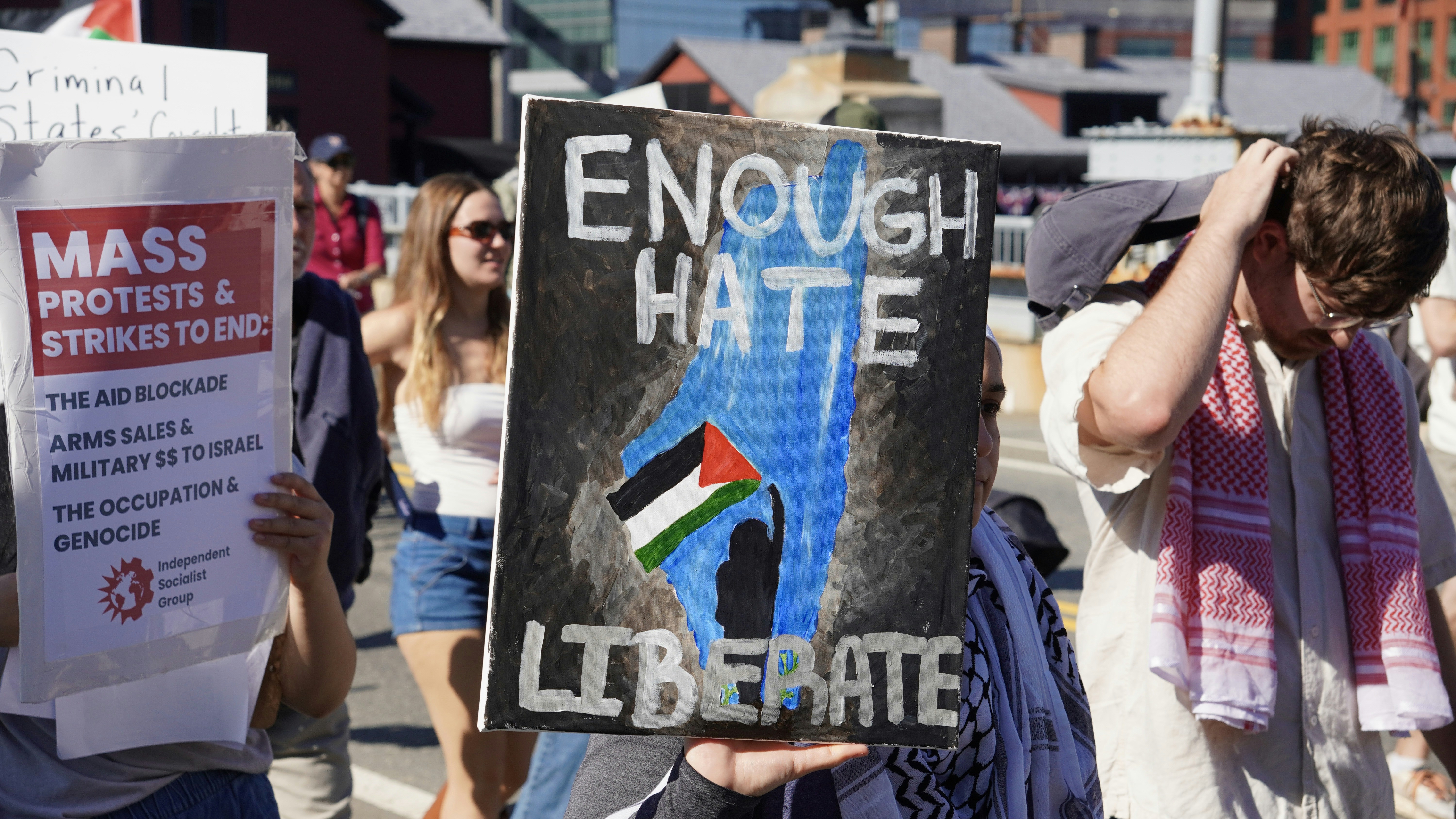 Protesters hold signs saying "enough hate liberate" and "mass protests"