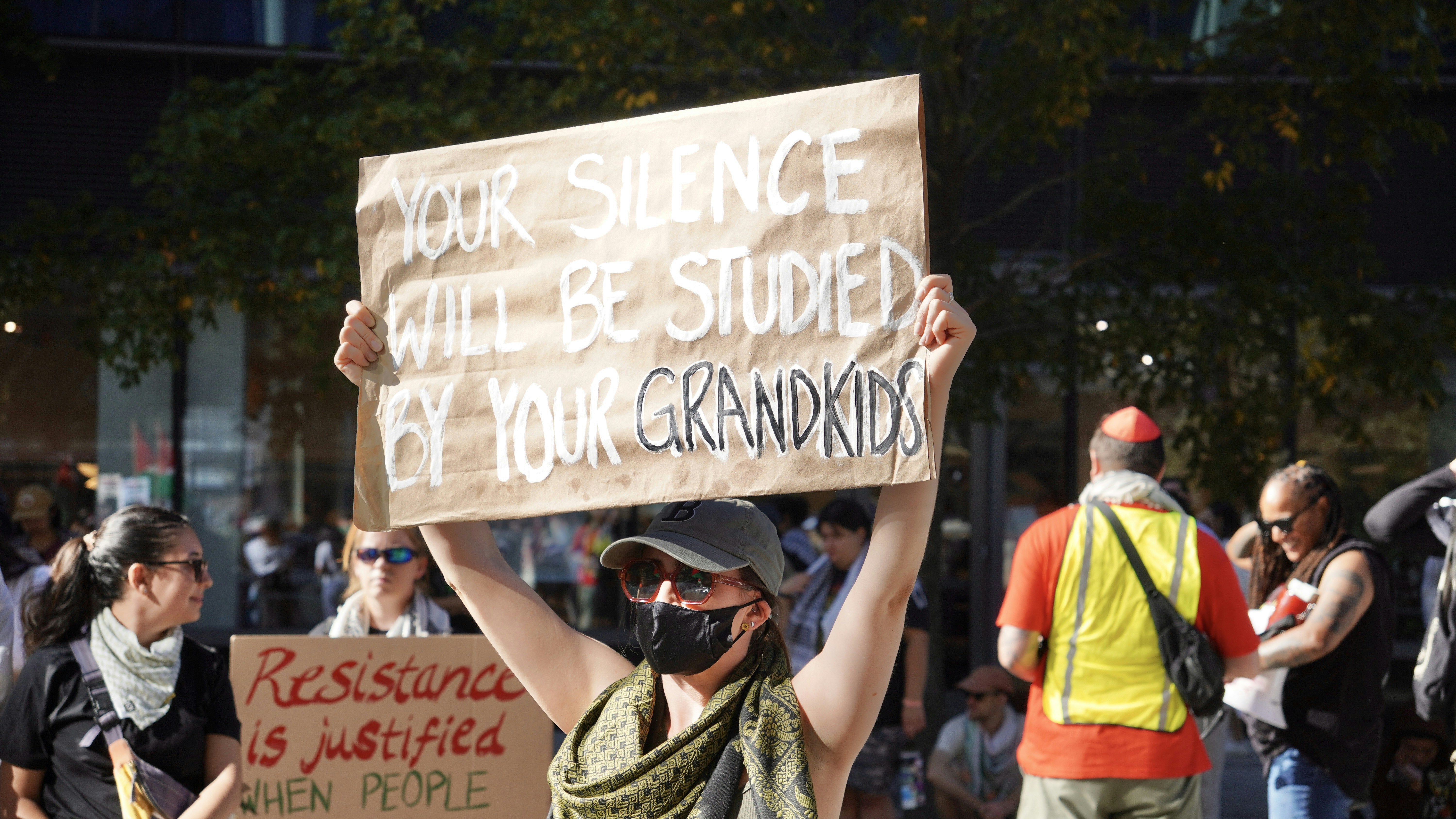Person holding protest sign about silence and grandchildren