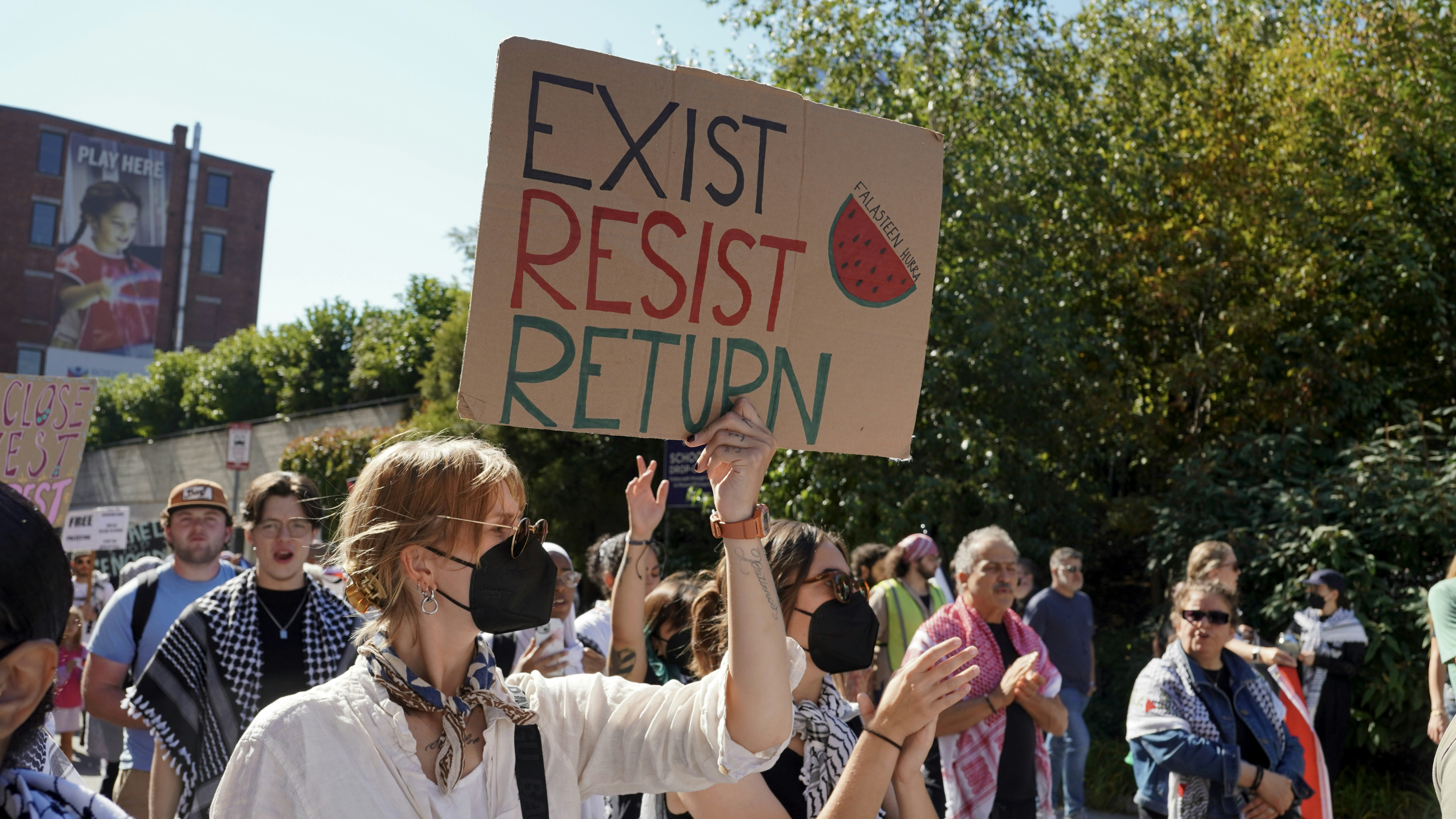 Protesters hold signs at a rally on a sunny day.