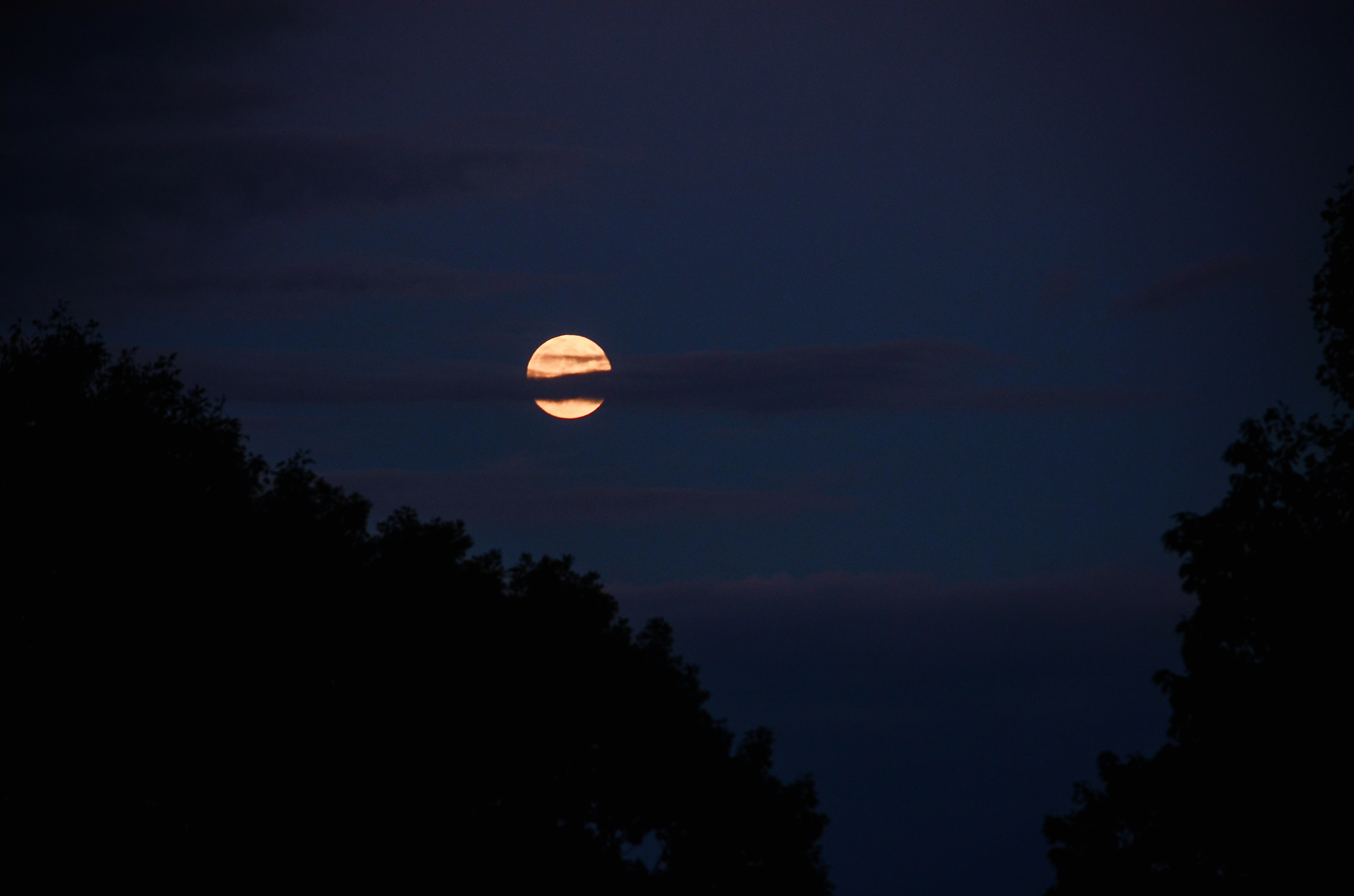 Full moon peeking through dark clouds at night.