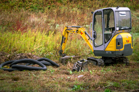 Mini excavator with coiled pipes on grassy ground
