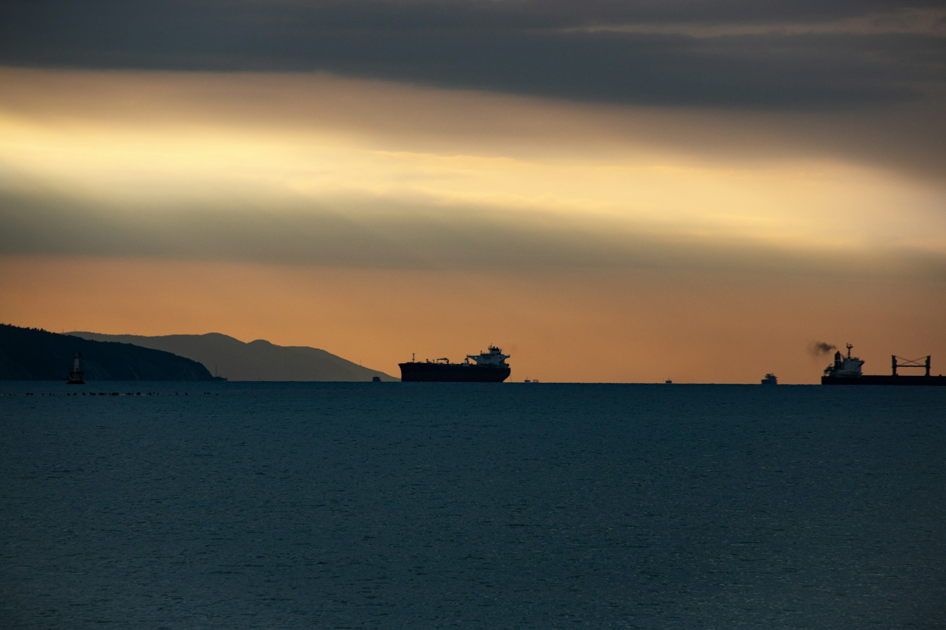 Ships on the ocean at sunset with mountains.