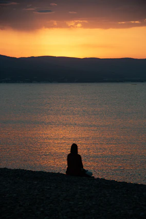 Silhouette of a person sitting by the ocean at sunset