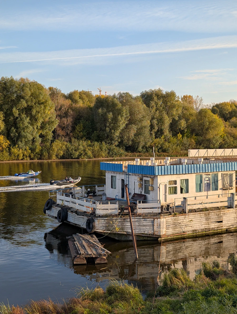 A DriftAway houseboat moored on a calm river lined with broadleaf trees