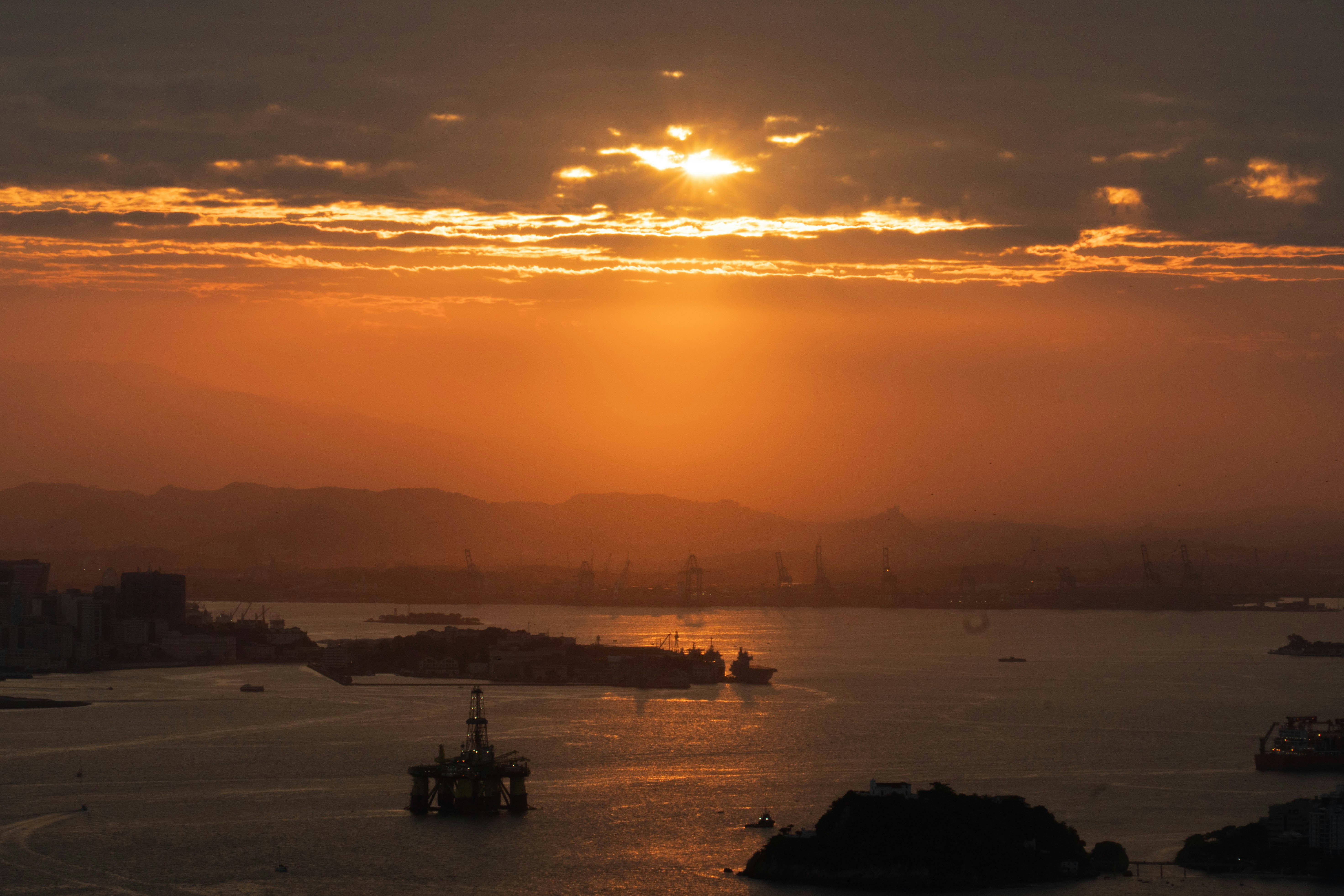 Sunset over a calm ocean with distant city lights.