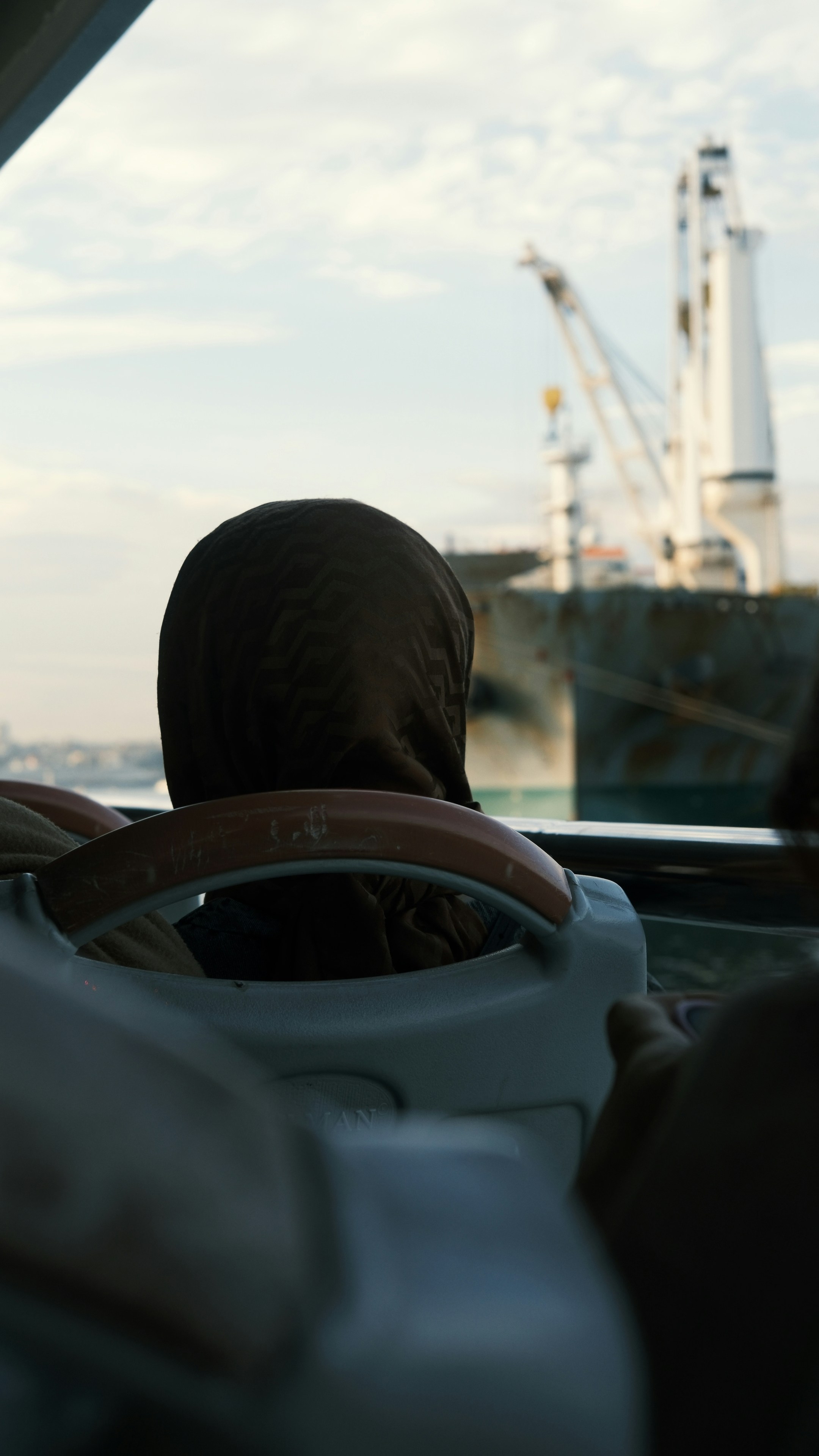 Woman wearing headscarf looks at large ship from window.