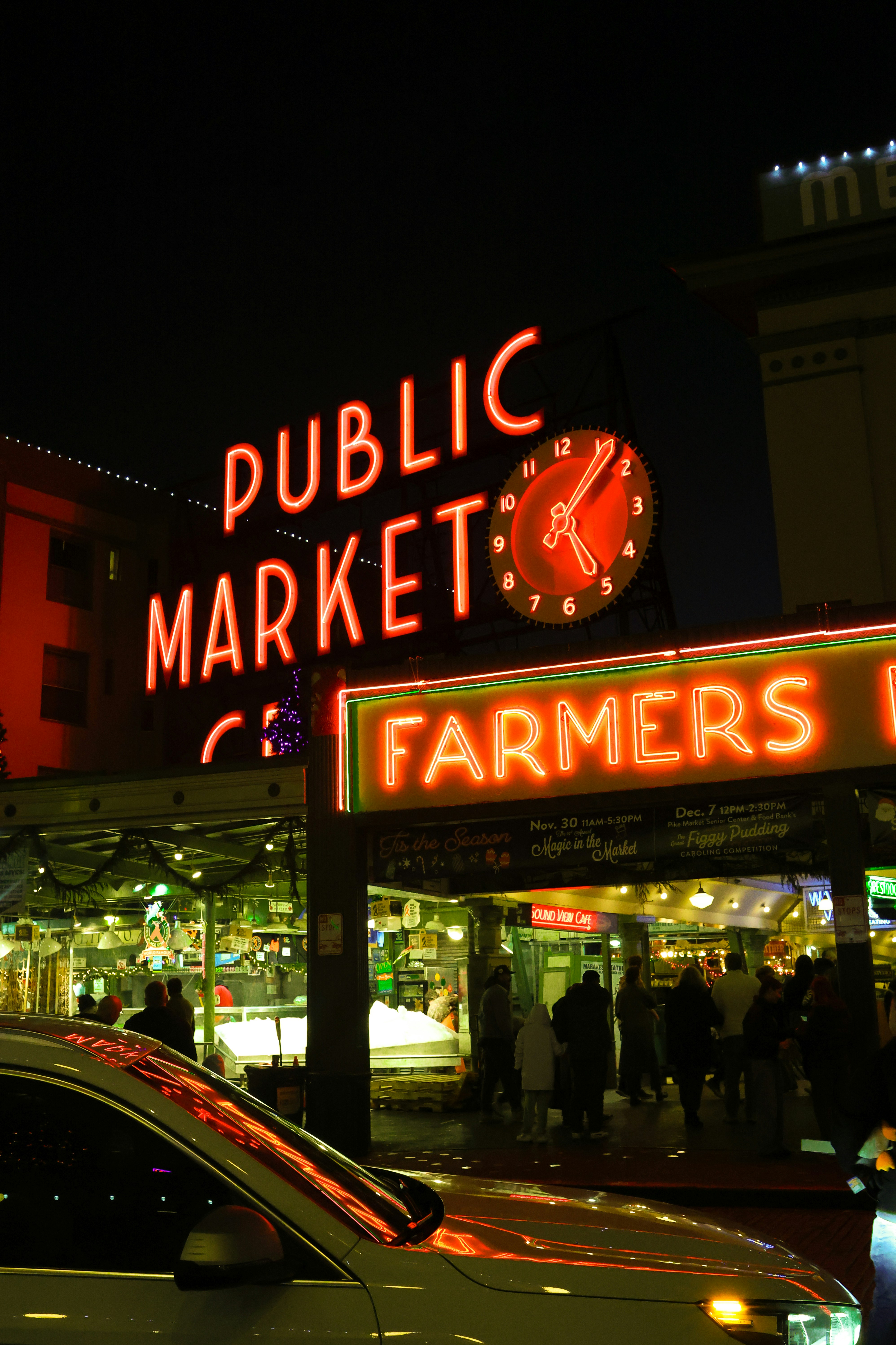 Neon signs glow at a bustling farmers market at night.