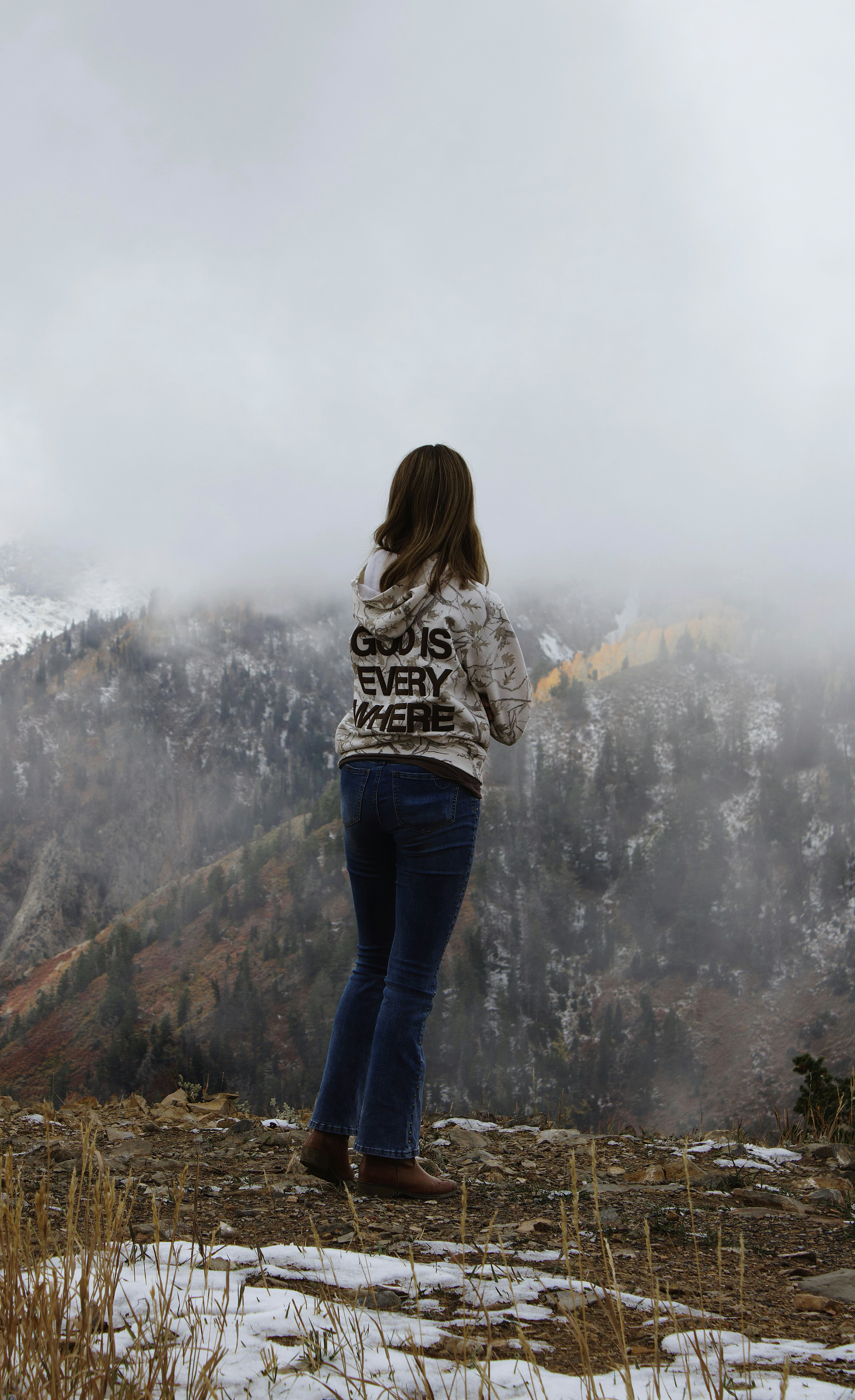 Woman in hoodie looking at misty mountains