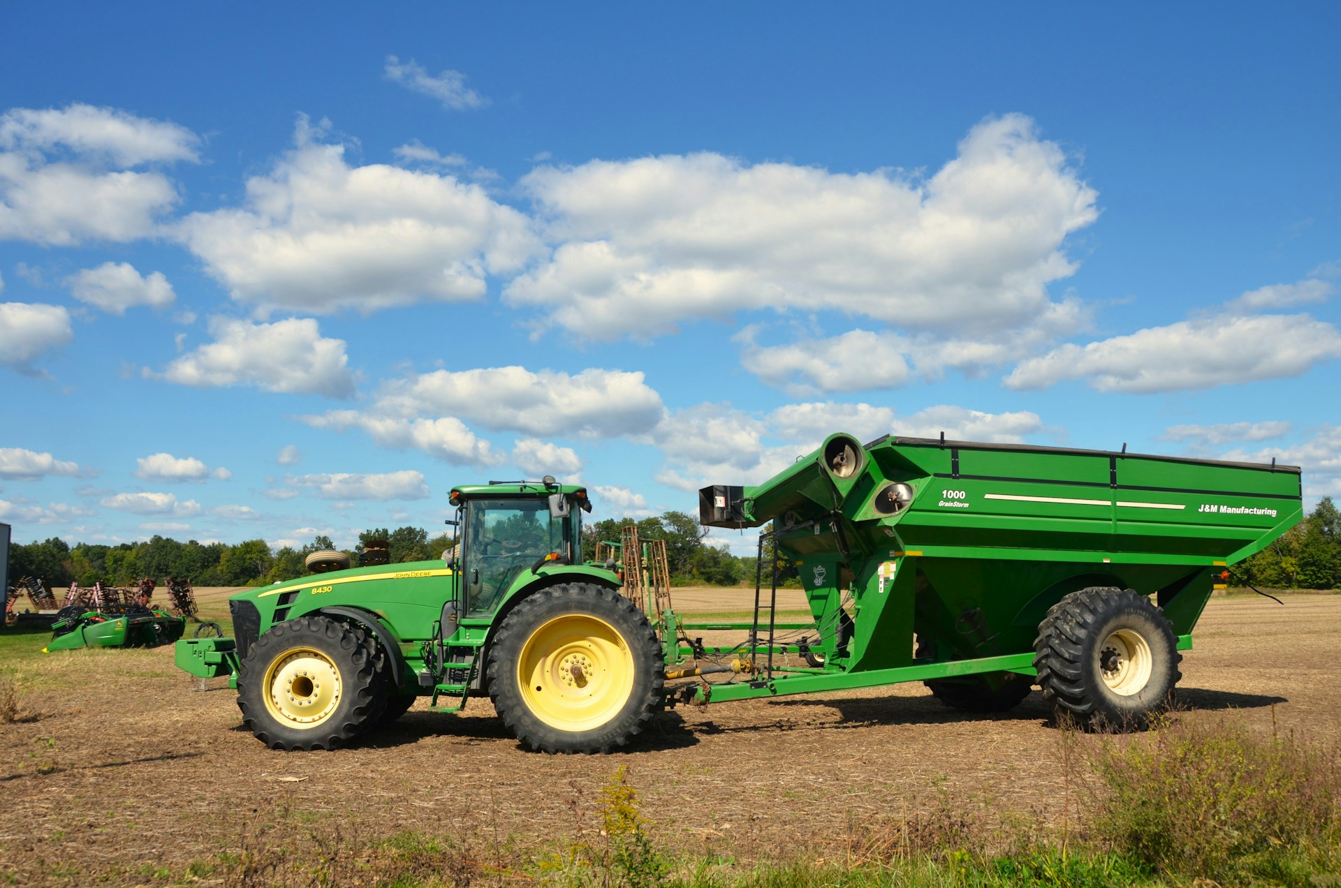 Green tractor pulling a large grain cart in a field.