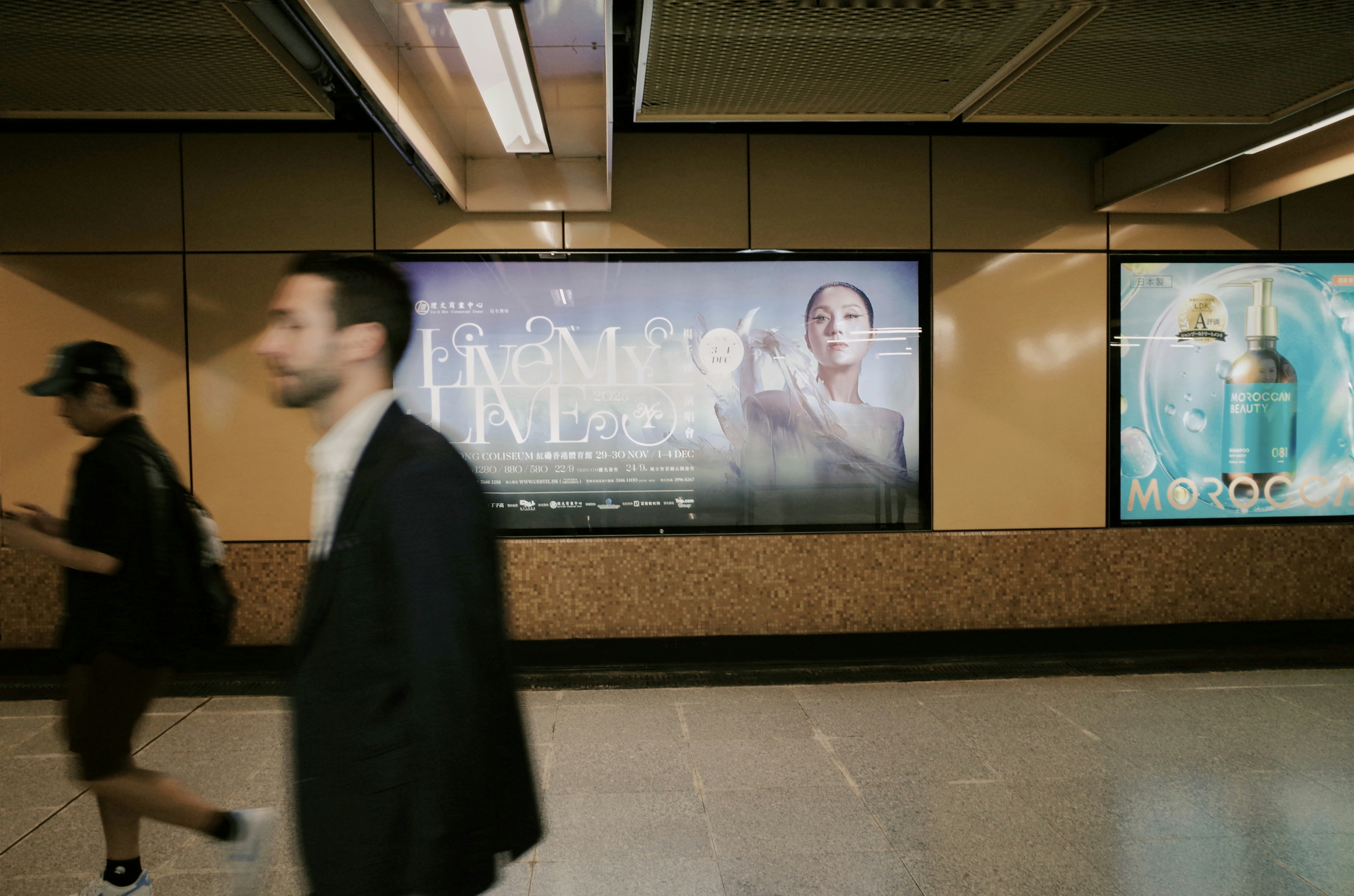 People walk past illuminated advertisements in a subway station.
