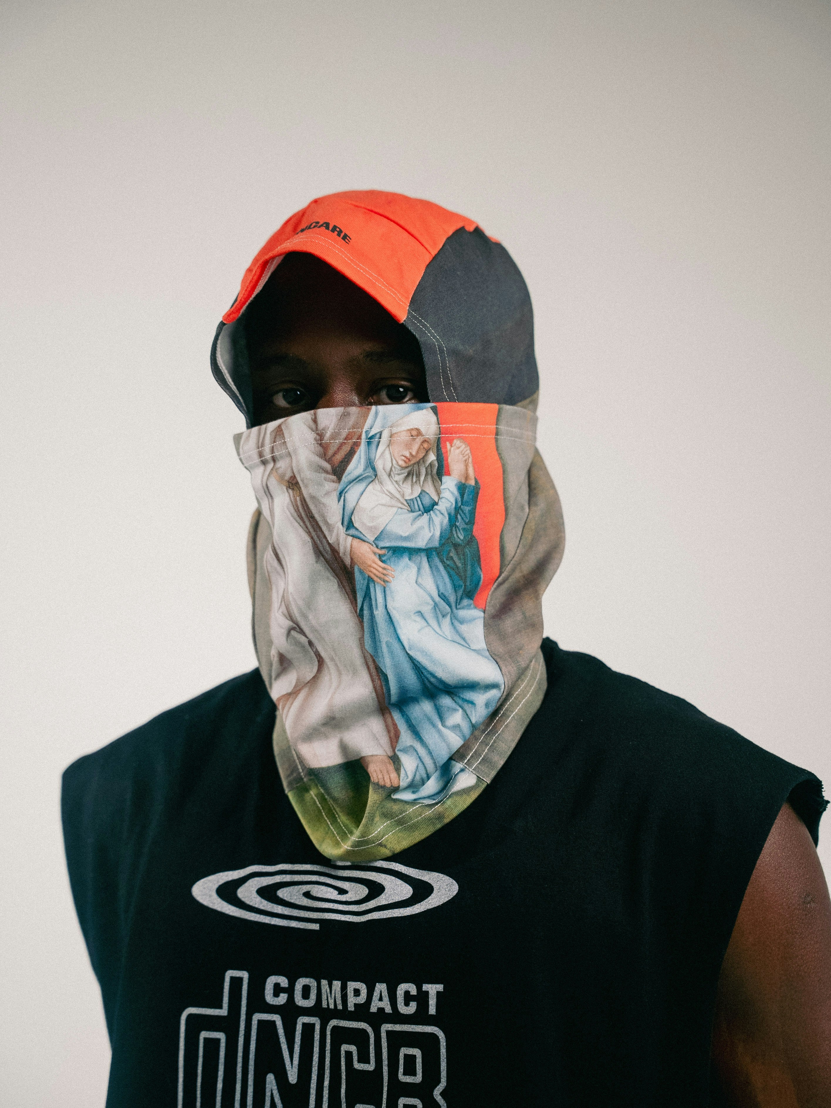 Person wearing a face covering with artwork and a hat.
