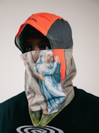 Person wearing a patterned face covering and orange hood