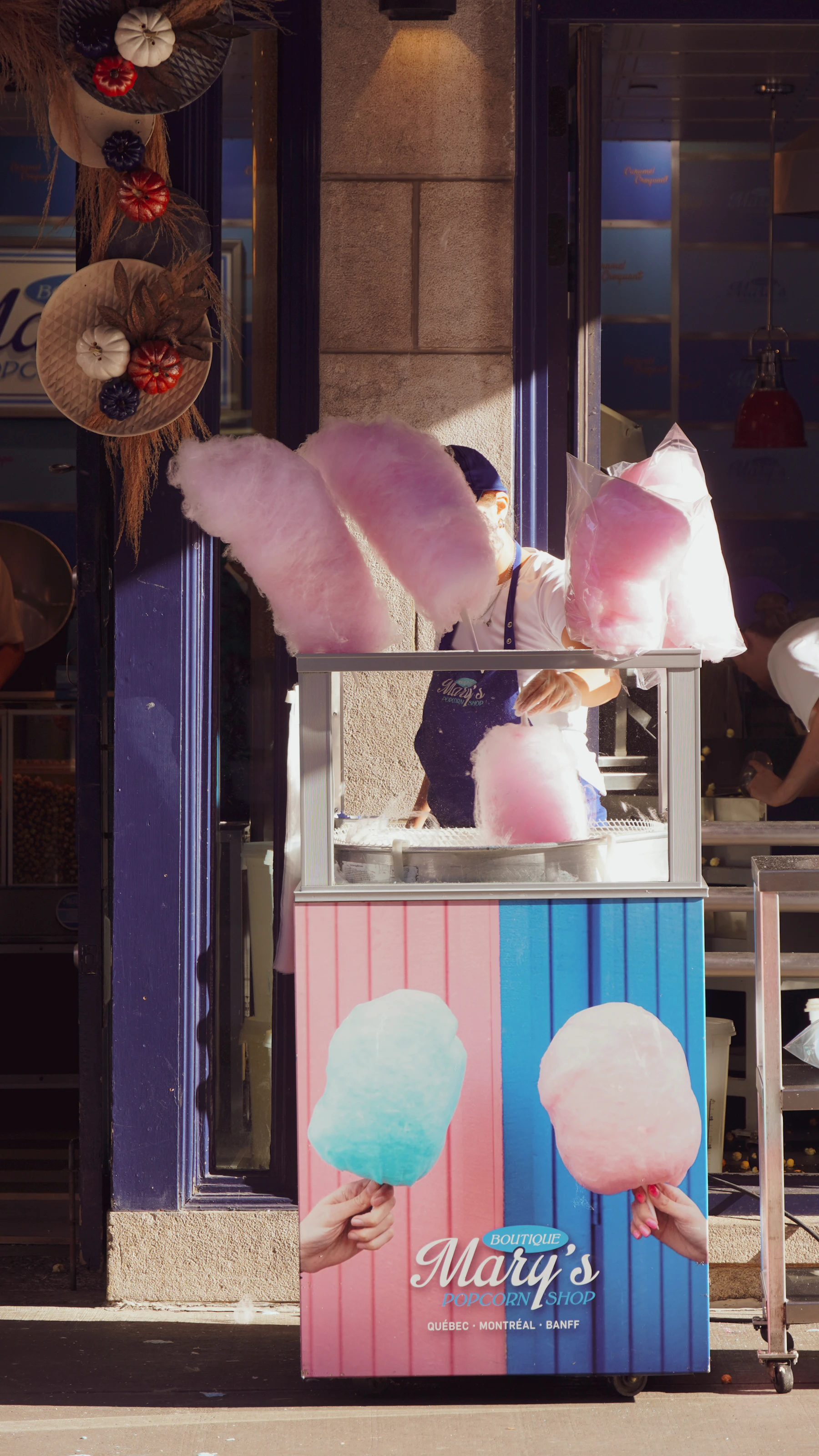 A street cart spinning pink cotton candy, with finished cones held up on display above the machine