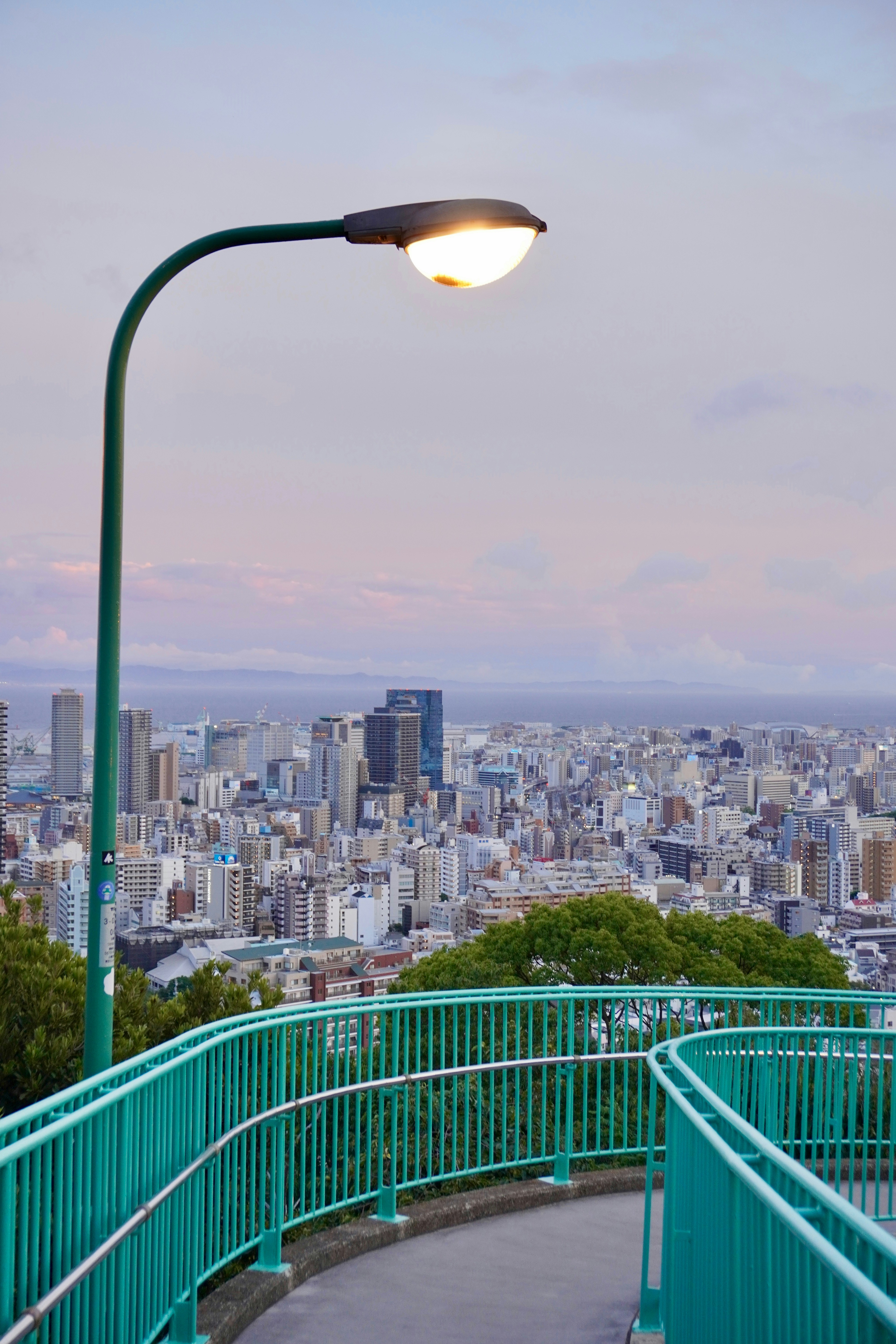 Green railing leads to city view with lamppost.