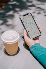 Person holding phone with coffee cup nearby