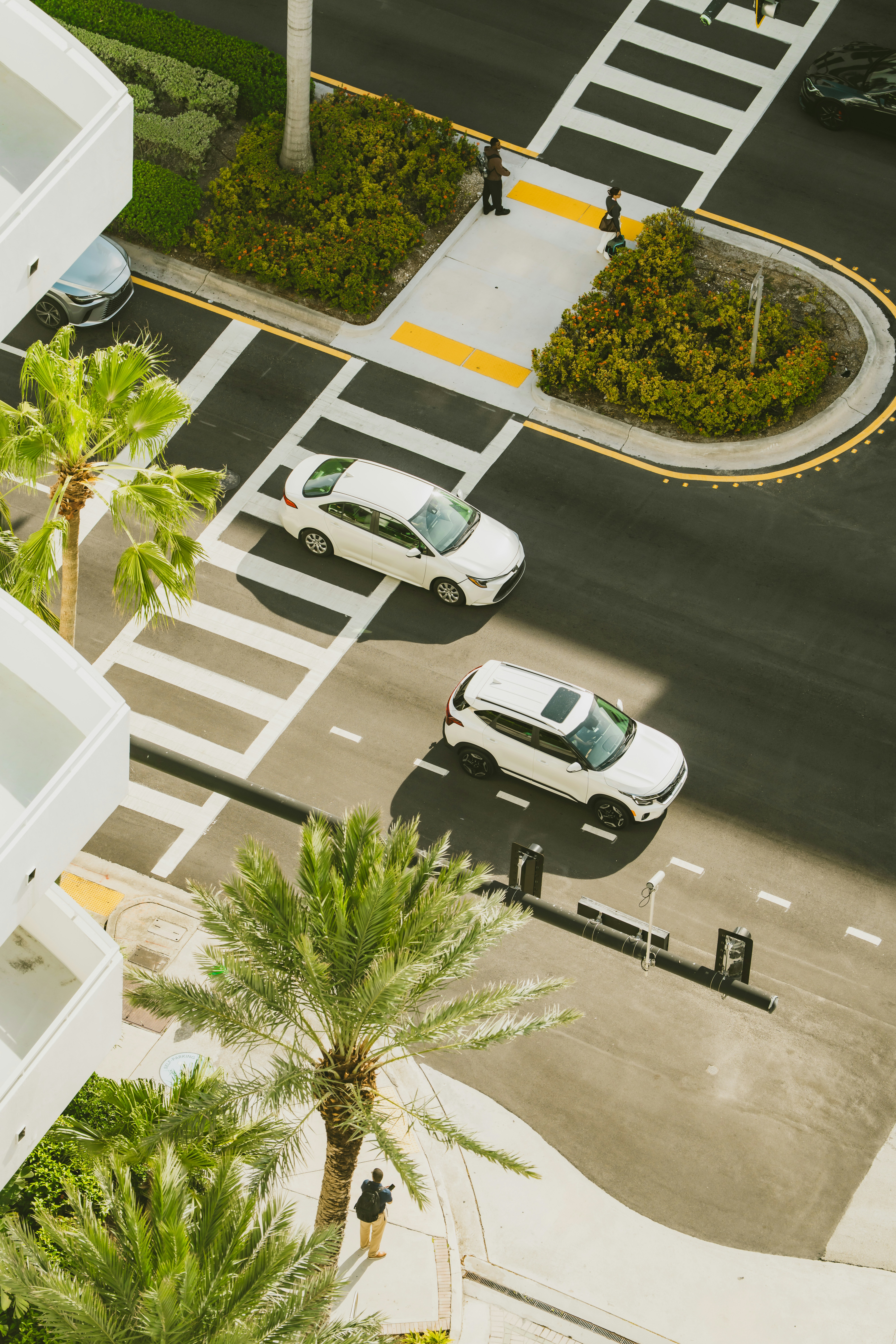 Two cars drive through a crosswalk on a sunny day.