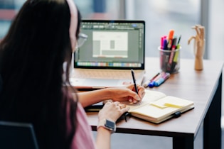 Woman working at a desk with laptop and notebook.