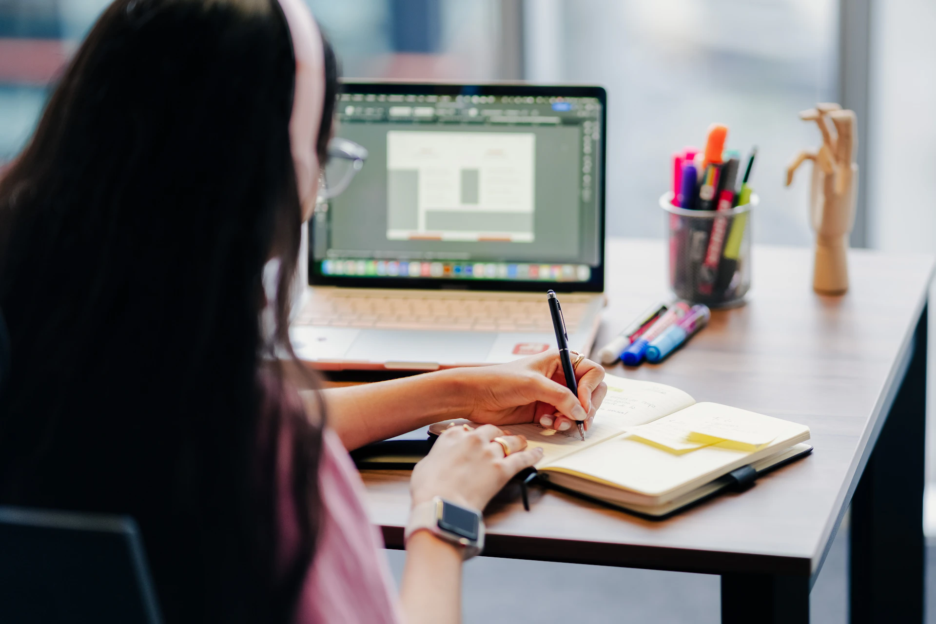 Woman working at a desk with laptop and notebook.