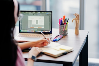 Woman working on laptop and notebook at desk.