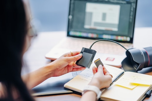 Person holding memory card near laptop and notebook.