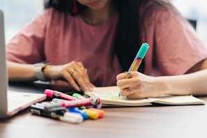 Woman writing in notebook with colorful markers nearby