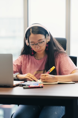 Young woman wearing headphones, studying at a desk.