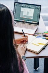 Person working on laptop and notebook at desk.