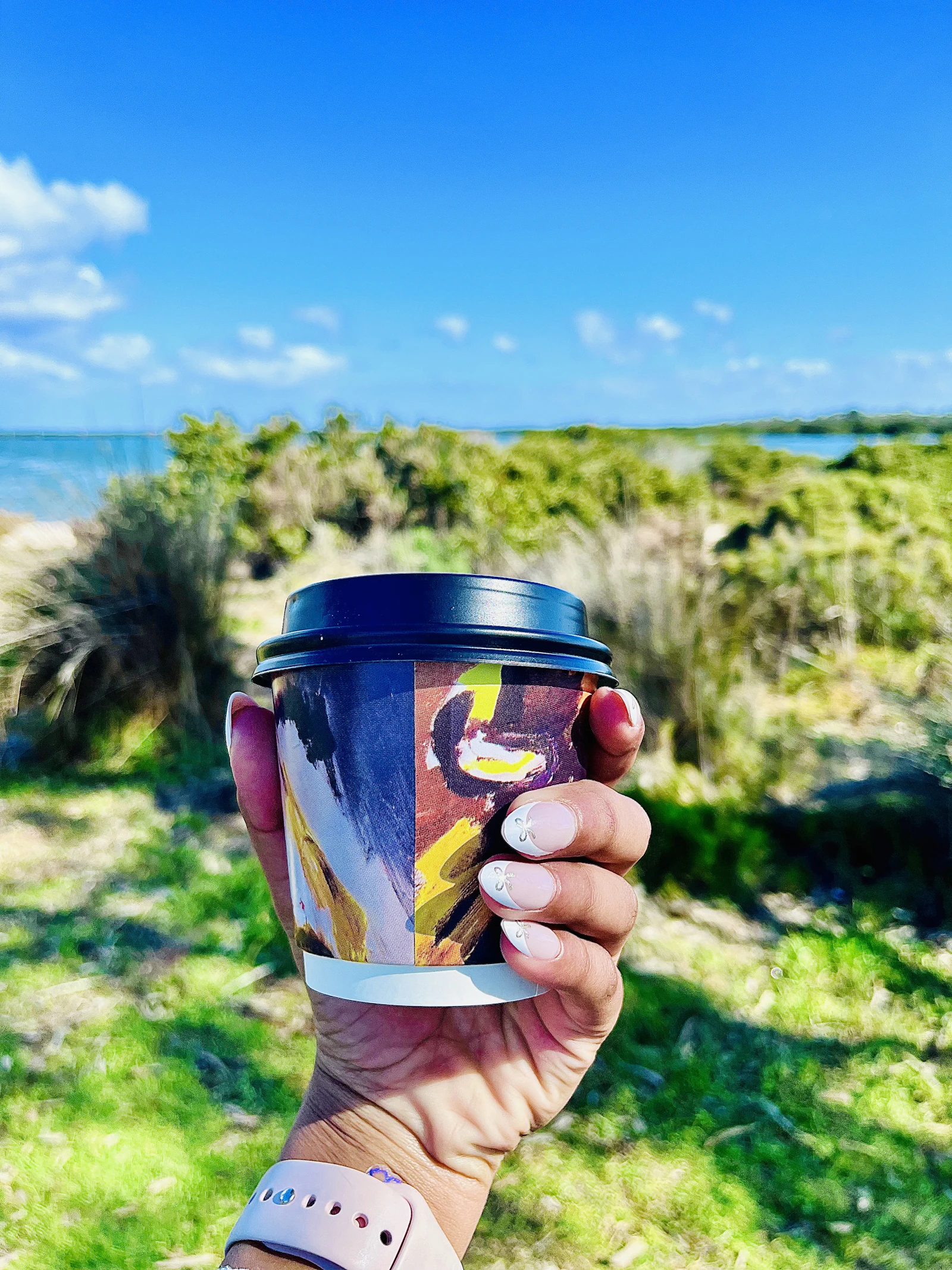Takeaway coffee cup held up against a sunny Irish coastline