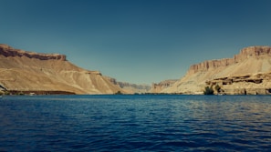 Blue lake between rocky desert mountains under clear sky