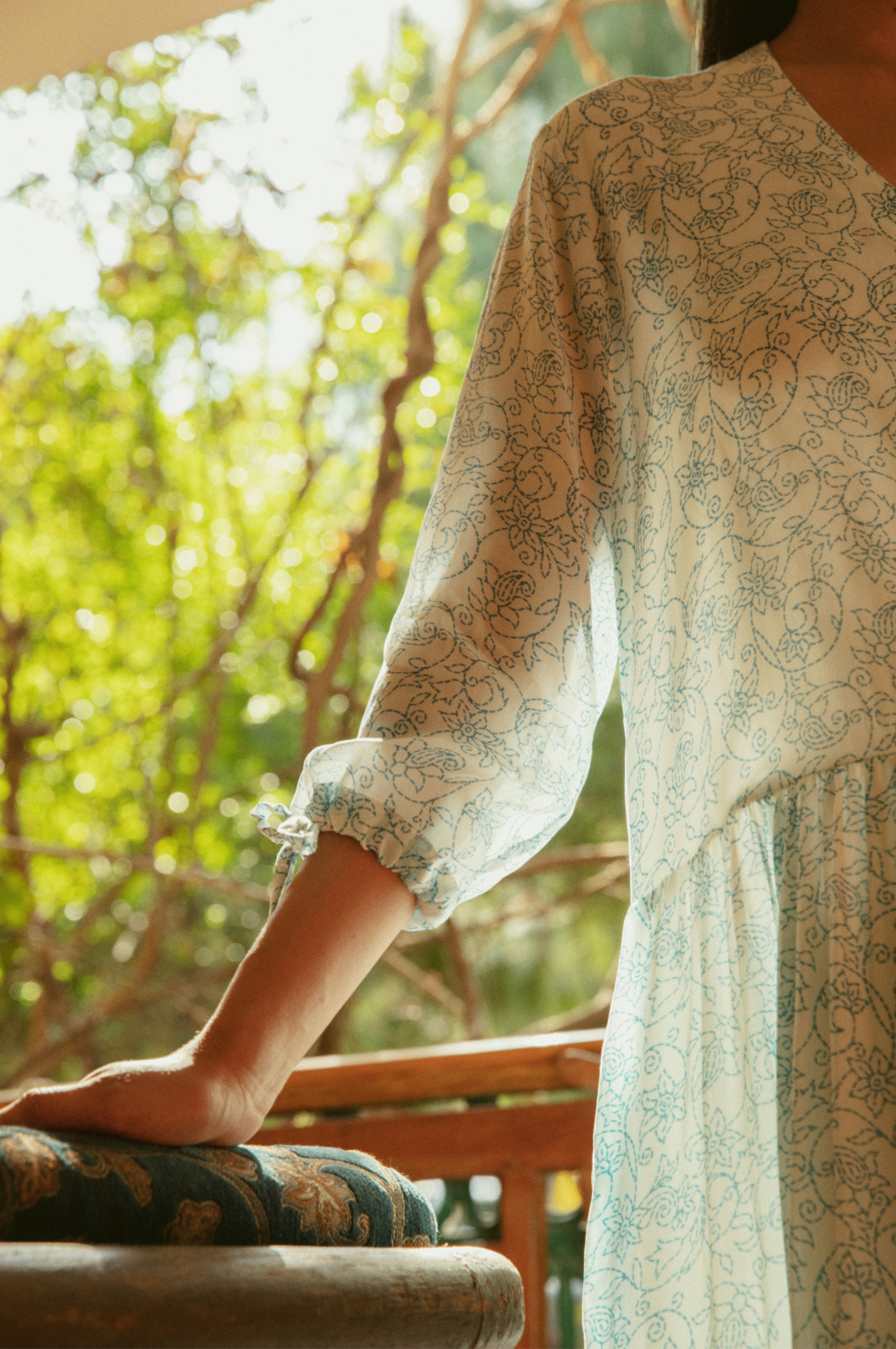 Woman in a light floral dress on a balcony.
