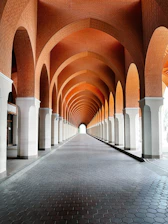 Long arched hallway with white columns and brick ceiling.