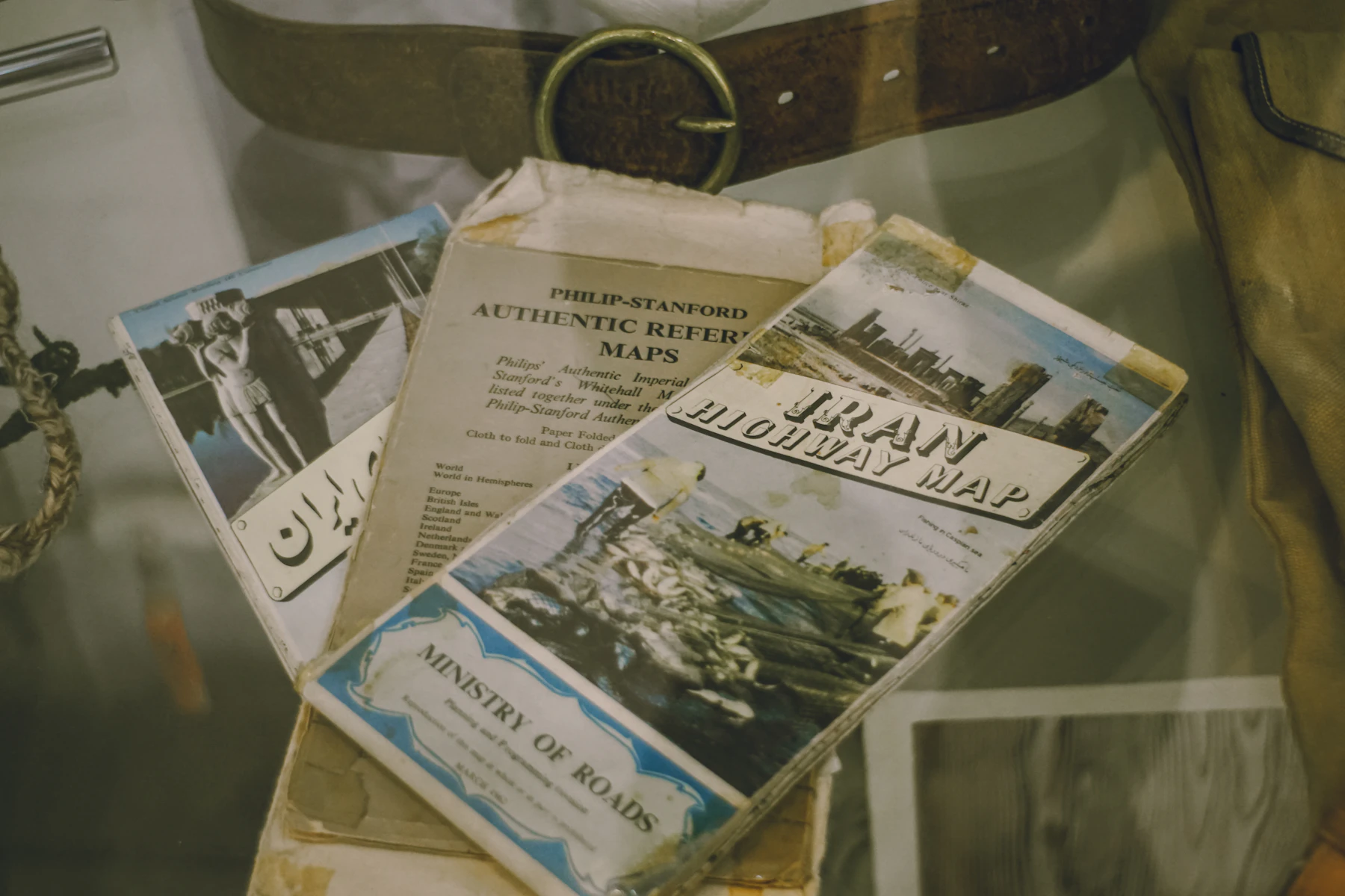 Folded highway maps and travel brochures with illustrated covers in a display case