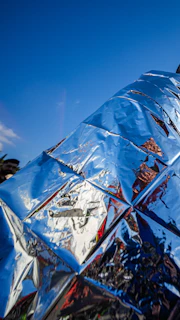 Shiny metallic surface reflects blue sky and red colors.
