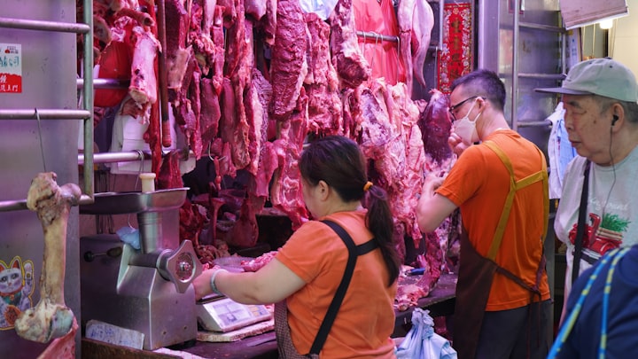 Butcher in apron working a meat counter beneath hanging carcasses, framed from the chest down
