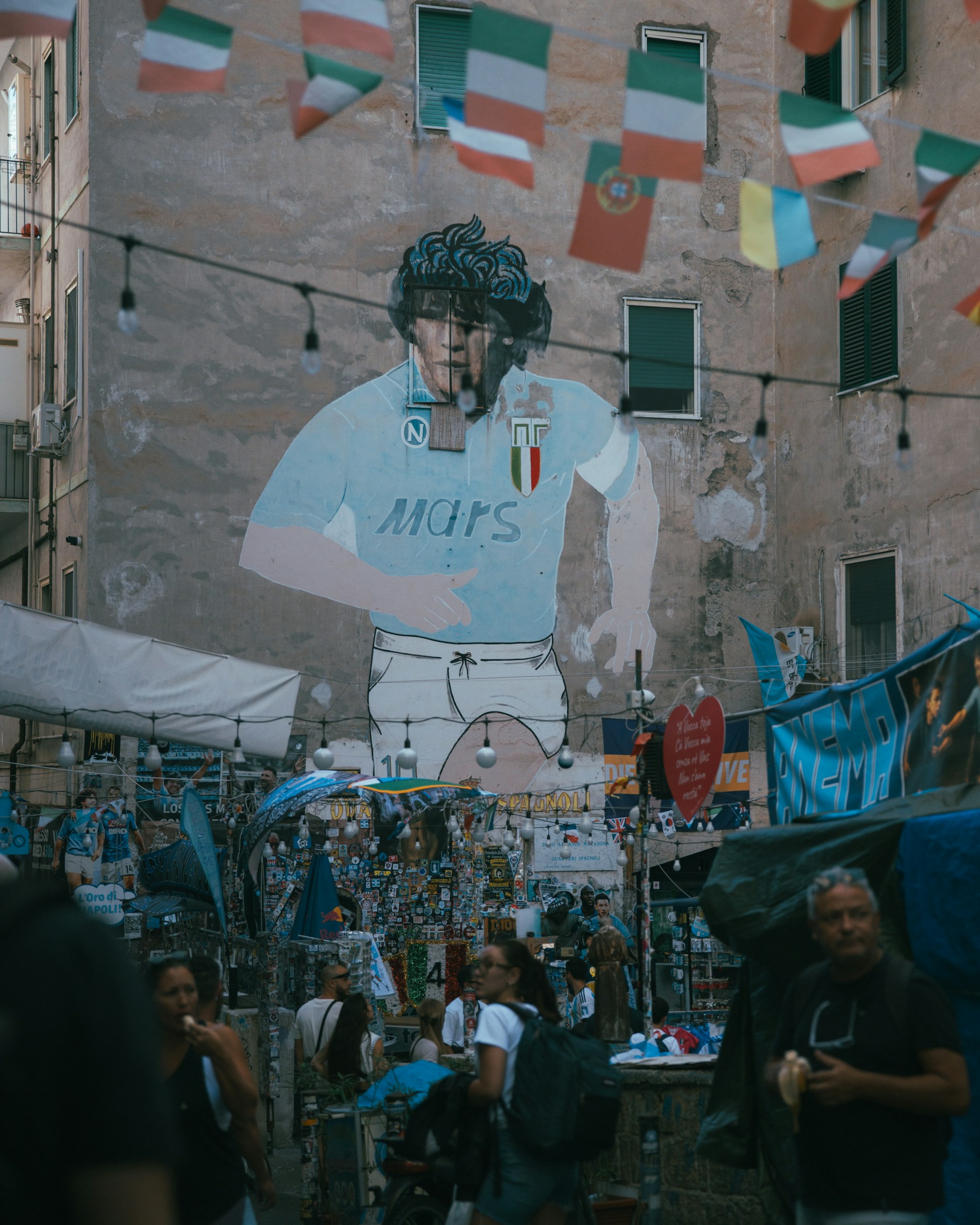 Mural of diego maradona with flags and people below.